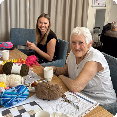 Aged care resident and carer knitting together.